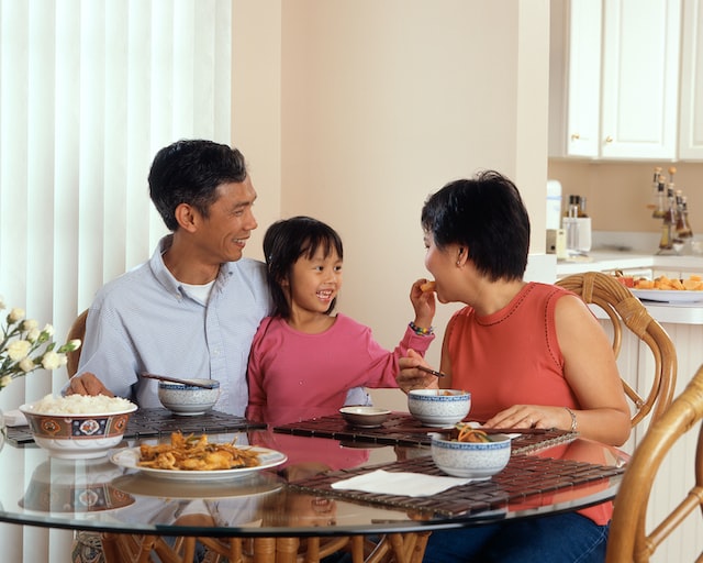 A man, woman, and little girl are seated around a table eating a meal.