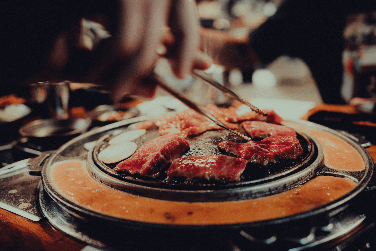 Pieces of steak are being grilled. Soup is around the edges of the grill.